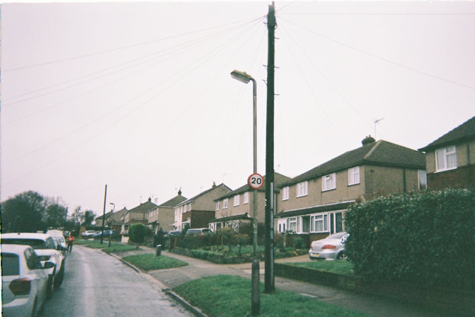 A residential street scene in North Ockendon, featuring a row of semi-detached houses with front gardens and driveways. Several parked cars are visible along the curb, including a silver hatchback nea